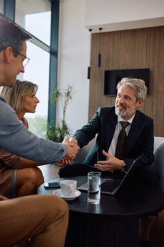 Happy financial advisor shaking hands with couple after successful meeting in office.