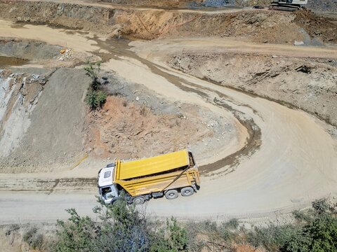 Aerial view of a yellow dump truck driving along a winding dirt road in a quarry with exposed earth and rocky terrain in Istanbul, Istanbul, Turkiye.