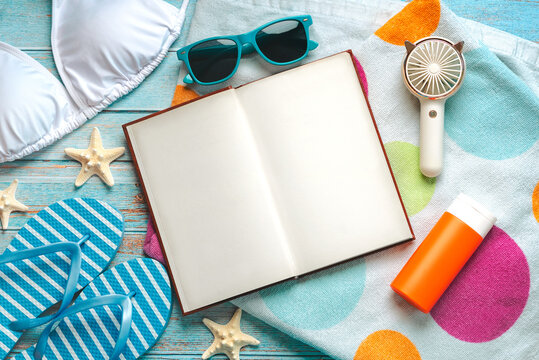 Top view of open book, flip flops, bikini,sunglasses and bottle of sunscreen