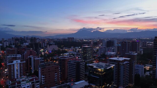 Postal panor&aacute;mica de la zona corporativa de Ciudad de Guatemala al crep&uacute;sculo con volcanes.