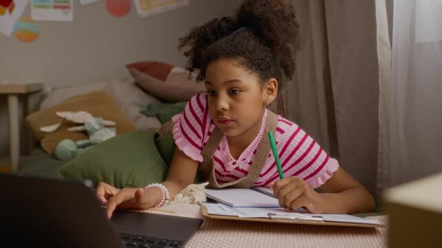 African American child writing in notebook and using laptop for online learning. Footage perfect for marketing digital education platforms and remote schooling services