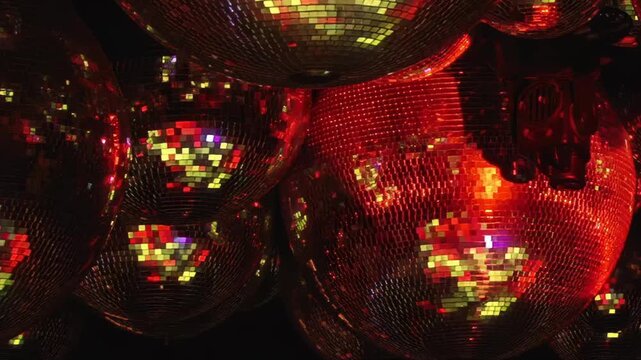 Multiple shimmering disco balls reflect an array of vibrant, changing colored lights, creating a dynamic and dazzling spectacle in a dark, energetic club environment during a festive night.