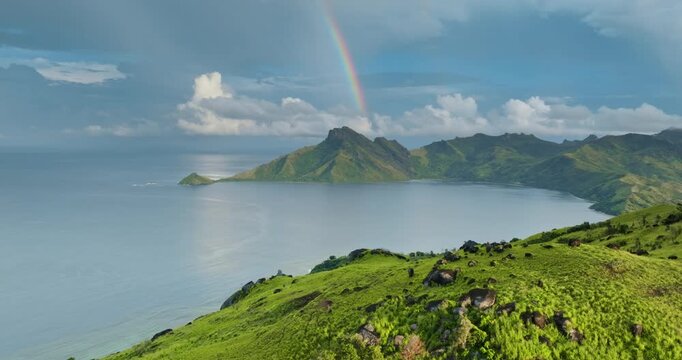 Vibrant rainbow arching over lush green mountains hills and serene bay, with vast Pacific Ocean meeting the tropical coastline of the Fiji Islands. Remote nature landscape. Aerial view drone panorama