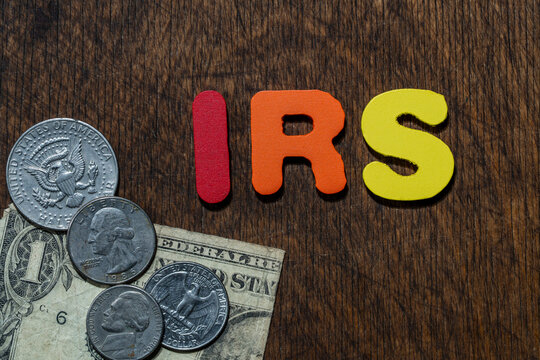 IRS letters with US dollars and coins on wooden background. Colorful IRS letters next American dollar bills and coins on wooden table representing taxation and financial system in United States