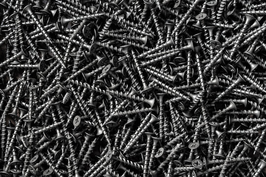Black drywall screws texture background, closeup. Macro shot of a pile of black metal screws for drywall and wood construction texture background top view