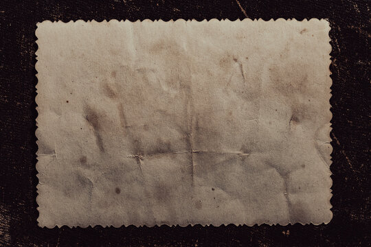 Blank vintage photo frame with wavy edges on dark background, closeup. Top view of an empty old textured paper card with scalloped edges isolated on dark brown grunge background copy space