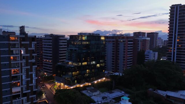 Vista panor&aacute;mica de Ciudad de Guatemala al atardecer con edificios corporativos y volcanes de fondo.