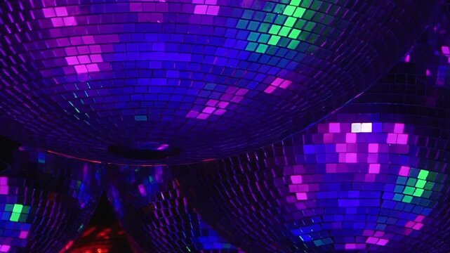 Mirrored spheres suspended in darkness catch and cast spectacular green, red, purple, and blue light across a lively club. This creates an electrifying atmosphere for a vibrant night celebration.