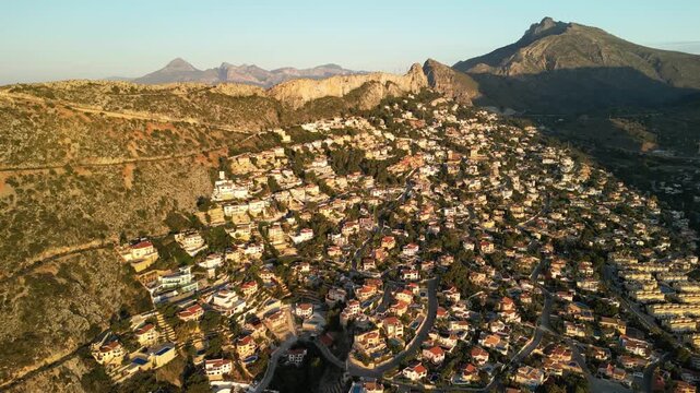 Stunning aerial panorama capturing a vibrant Mediterranean town nestled against rugged hills, stretching towards the shimmering coastline under the golden glow of sunrise. Calpe, Costa Blanca, Spain