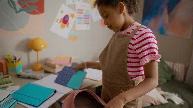 African American girl packing backpack with school supplies and homework in bedroom. Clip perfect for back-to-school marketing, educational campaigns, and parenting content