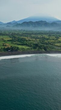 Aerial panoramic farmland volcano agung expansive rice plots and coastal rim, distant misty peaks and calm ocean, rural mosaic of ponds and cultivation under soft light,Bali,Indonesia