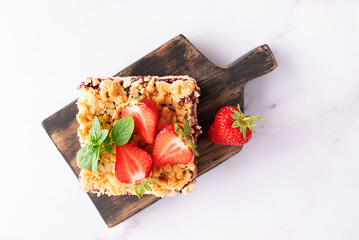 Sweet homemade pie with strawberry jam, decorated with fresh strawberries and aromatic herbs on the wooden tray onwhite marble table top view. © Iryna