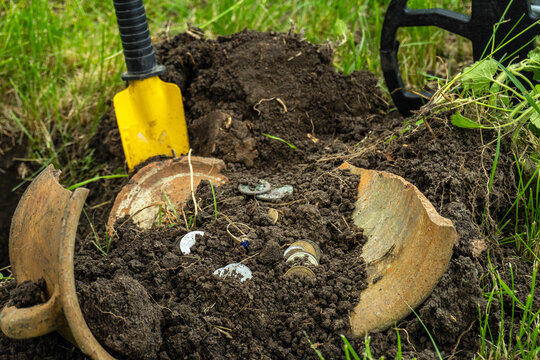 Searching for buried coins and artifacts with a metal detector in a grassy field. Broken clay pot with silver coins and gold artifacts or treasure