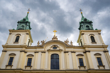 Baroque church in Warsaw with gilded cross, angels and ornate facade under dramatic spring sky © Luis