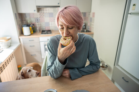 Mature woman having sugar abstinence breakdown, biting glazed doughnut, guilty pleasure and uncontrolled overeating sweets during stress, female with compulsive food disorder eating sugar pastries.
