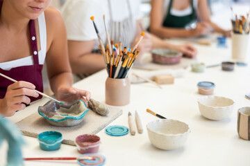 Close up of female hands painting ceramic plate with paint and brush in pottery workshop © JackF