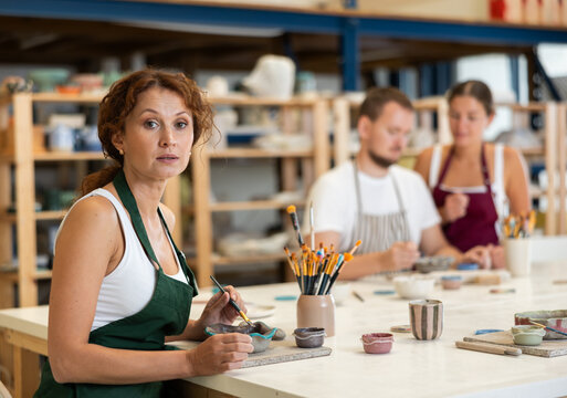 Woman learns to make designs on clay plate using brush and paint in a pottery workshop