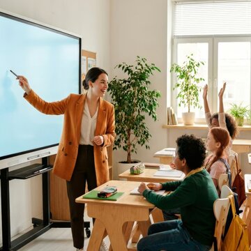 Female teacher using interactive smart board in classroom. Elementary school students raising hands during lesson