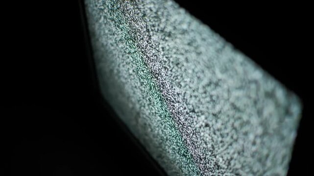 Macro detail perspective captures television static noise flickering intensely. The screen shows a dense pattern of white and black dots resulting from lost signal or analog interference effect.