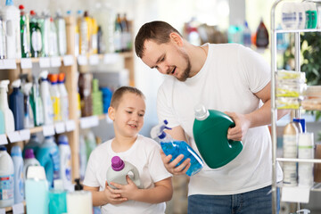 Obraz premium Boy and father in process of choosing bleaching agent, looking at packages, reading labels on packages. Family shopping in household department, pick up household chemistry during store routine buying