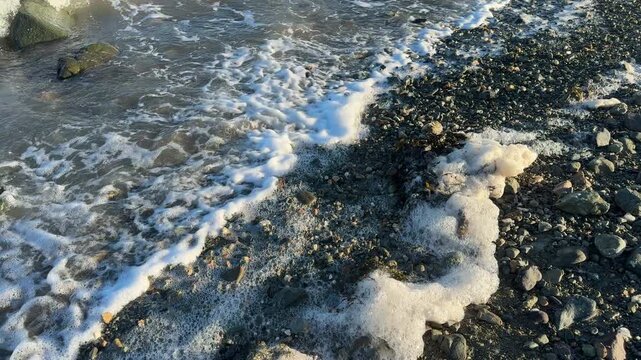 Aerial view of waves and surf moving over shingle beach with foam close up view UK 4K