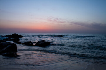 Fototapeta premium Serene ocean waves gently lap against dark rocks at twilight