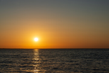 Fototapeta premium Stunning vibrant sunset over the ocean horizon, with the bright sun casting a glowing golden reflection across the gentle ripples of the sea surface in a peaceful evening atmosphere.