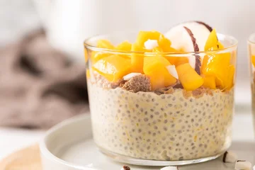 Creamy chia seed pudding in a glass topped with vibrant yellow mango cubes and fresh coconut slices for a healthy breakfast or tropical vegan dessert on a neutral aesthetic background with no marks © anammarques
