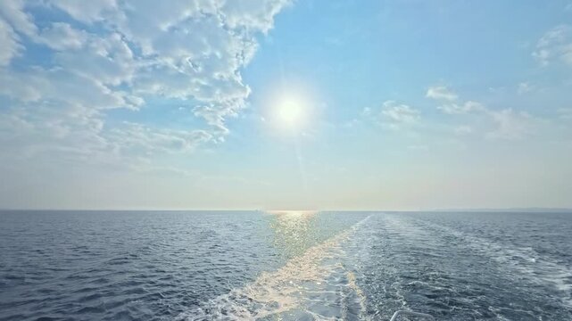 Majestic cloudscape and sun rays over the ocean with white foam from a cruising vessel