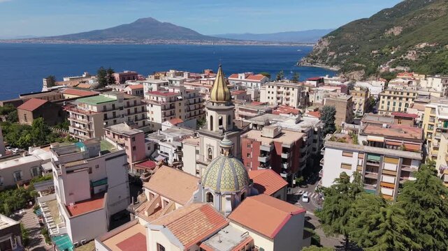 Aerial view of Vico Equense old town with Chiesa dei Santi Ciro e Giovanni golden dome, colorful buildings and Mount Vesuvius across Gulf of Naples, Italy
