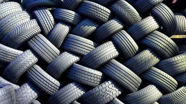 Stacked used tires in a herringbone pattern, Brooklyn, New York. Full frame close up of interlocking black rubber treads with varied grooves and sunlight.