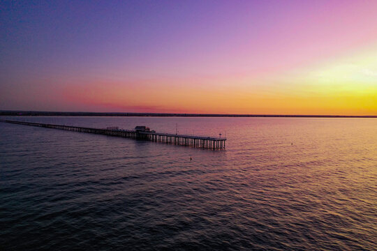 Aerial view of Busselton Jetty extending into the calm ocean waters during a vibrant sunset with purple and orange sky in Busselton, Western Australia, Australia.