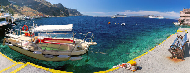Panoramic view of a small boat moored in the clear waters of Ammoudi Bay with cruise ships anchored in the Santorini caldera. © Kavalenkava