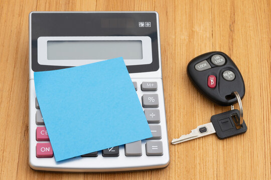 Calculator and car keys and sticky note and pen on wood desk