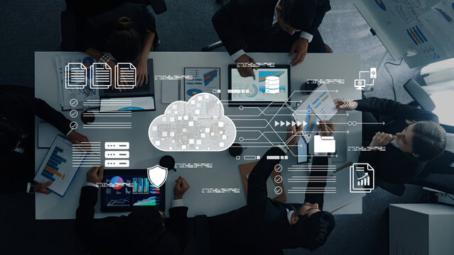 A modern business meeting showcasing cloud technology and data analysis. Professionals collaborate around a table with devices, charts, and graphs, highlighting digital transformation. Cyphers