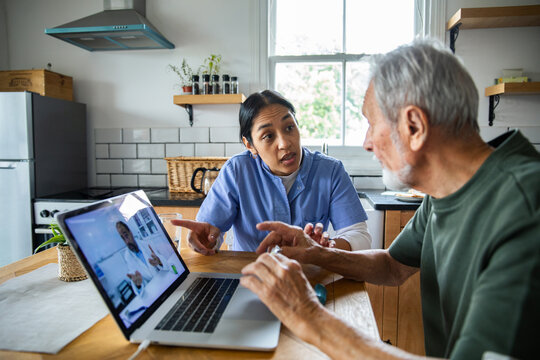 Caregiver assisting senior man with telehealth video consultation at home
