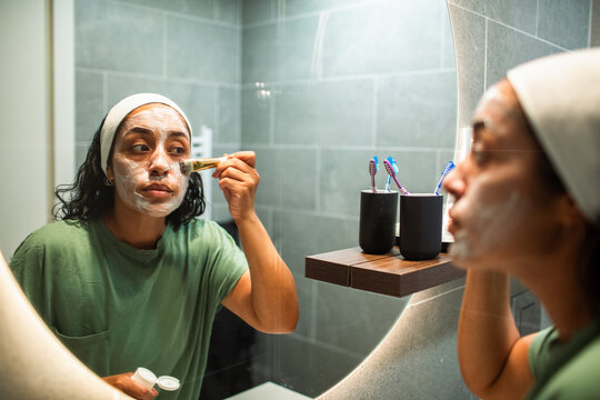 Woman applying facial mask in bathroom mirror
