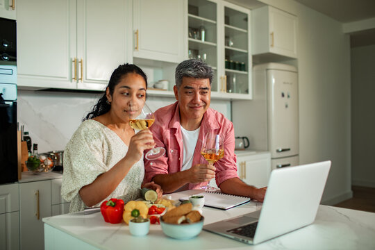 Couple enjoying virtual wine tasting and cooking in home kitchen