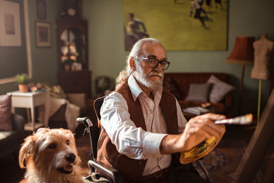 Senior man in wheelchair painting at home studio with dog