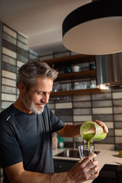 Mature man pouring green smoothie in home kitchen