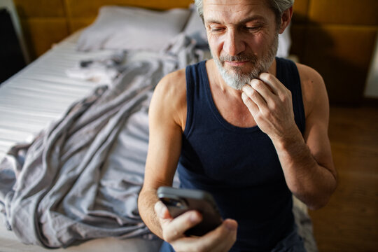 Mature man checking smartphone in bedroom at home