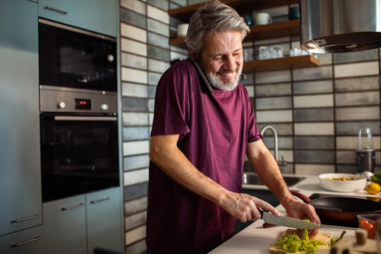 Smiling senior man cooking while talking on phone in a home kitchen