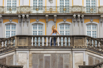Obraz premium Woman stands on balcony of building with yellow and gray walls during daytime