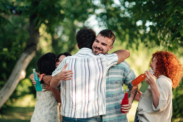 Fototapeta premium Happy friends embracing at outdoor park gathering, sharing drinks during a joyful reunion celebration