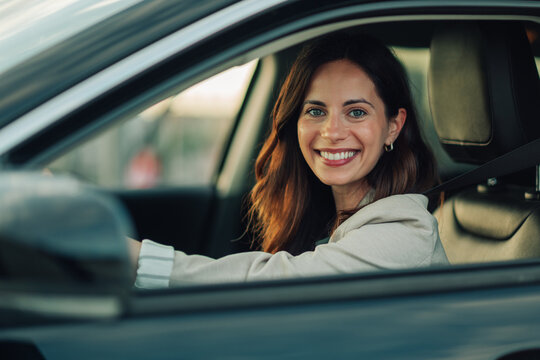 Happy woman driver smiling from car window, feeling joy and freedom while commuting or traveling in a modern vehicle