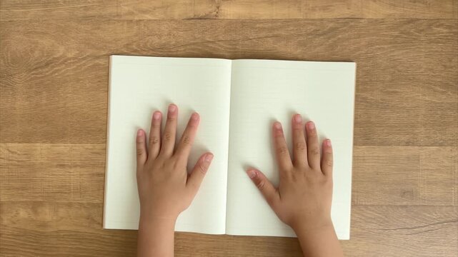 Child Hands Slide an Open Notebook Slightly Forward on a Wooden Table, 4K