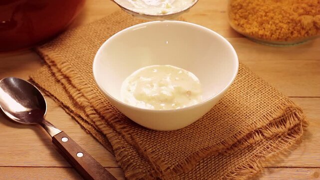 Traditional Brazilian creamy canjica or mungunza being served in a white bowl on a rustic wooden table