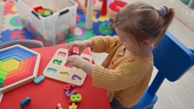 Girl placing wooden puzzle pieces with hands at a small red table and rainbow stacker visible in a building; concentration learning.