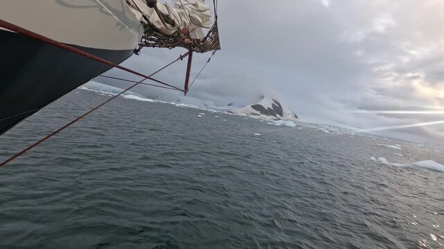 POV shot tracking along the bow of a ship sailing through dark, choppy ocean waters filled with icebergs and ice chunks under cloudy skies at Wilhelmina Bay, Antarctica