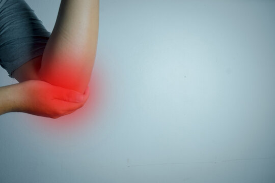 Close up of person holding painful elbow with red highlight indicating joint inflammation. Tennis elbow, repetitive strain injury, and orthopedic physical therapy concept banner with copy space.